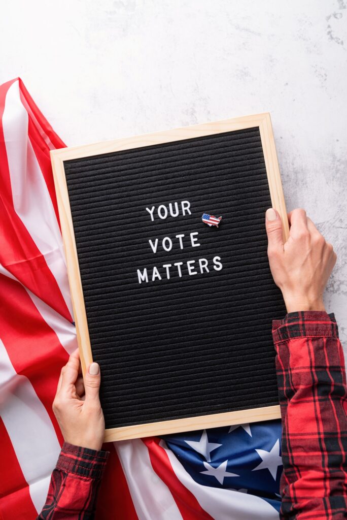 Letterboard sign with the words your vote matters with American flag on white marble background