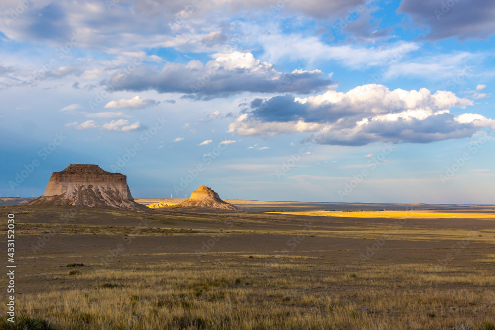 Pawnee Buttes in Pawnee National Grassland, on the great plains of Colorado with clouds forming against a blue sky and the sunlight highlighting  one area of the landscape